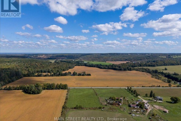 Drone shot of agricultural fields, a farmhouse, barns, and surrounding forest. - 5427 Hogg Valley Road, Tay