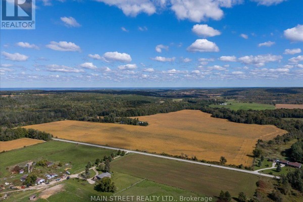 Expansive farmland with a house and outbuildings, bordered by trees and a country road. - 5427 Hogg Valley Road, Tay