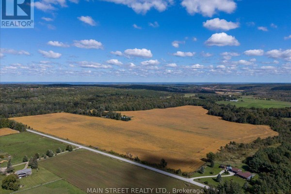 Overhead view of yellow farm fields, green pastures, a long driveway, and dense woods. - 5427 Hogg Valley Road, Tay