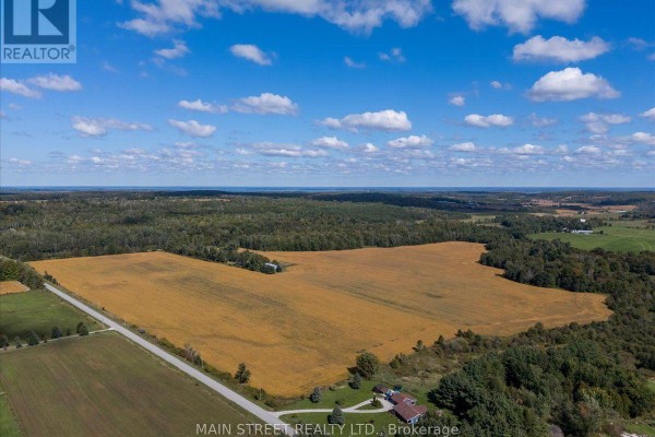 A sweeping aerial perspective of cultivated fields, farm structures, and a forested landscape. - 5427 Hogg Valley Road, Tay