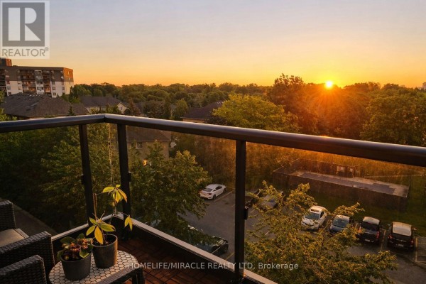 Balcony view at sunset with a sunburst over trees, cars, and apartment buildings. - 543 - 26 Gibbs Road, Toronto