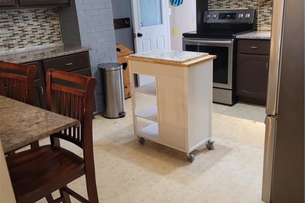 Kitchen with dark cabinets, stainless steel appliances, a mobile island, and dining chairs with dark wood. - 543 Champlain Street, Dieppe