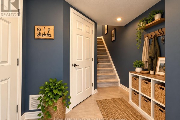 Hallway with a blue wall, beige tile floor, and carpeted stairs leading up. - 543 Ensatina Crescent, Ottawa