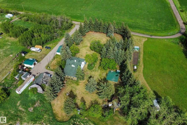 Aerial view of a cluster of buildings and trees on a property, surrounded by green fields and some trailers. - 54318 Rge Rd 255, St  Albert