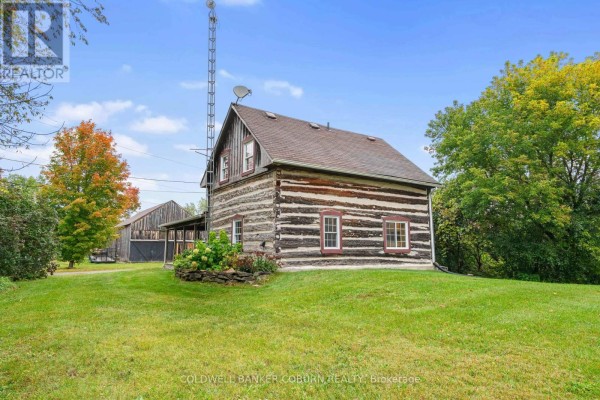 Log cabin exterior with a metal radio tower and surrounding green lawn and trees. - 544 Craig Road, North Grenville
