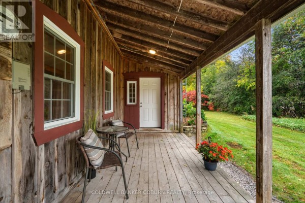 Covered wooden porch with two chairs, a table, and a white door with red trim. - 544 Craig Road, North Grenville