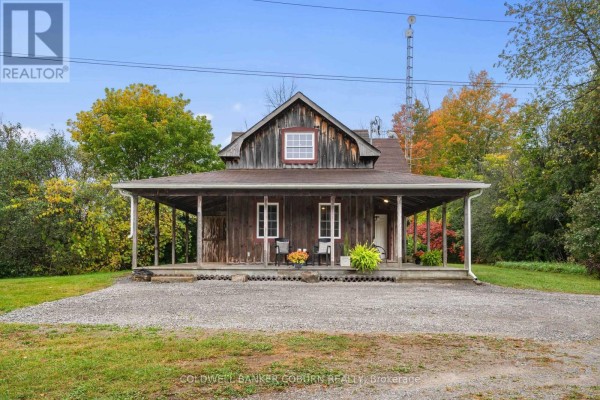 Front view of a weathered wooden house with a wide covered porch and gravel landscaping. - 544 Craig Road, North Grenville