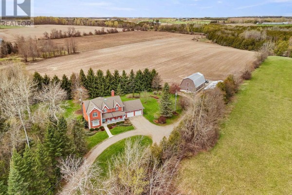 Front view of a red brick house with a white porch, white trim, and an attached three-car garage. - 5445 5th Line, Guelph/eramosa