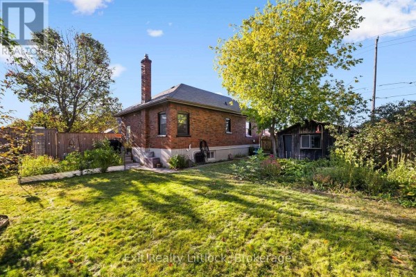 Backyard view of the brick house with a grassy lawn and a small wooden shed. - 545 Braidwood Avenue, Peterborough