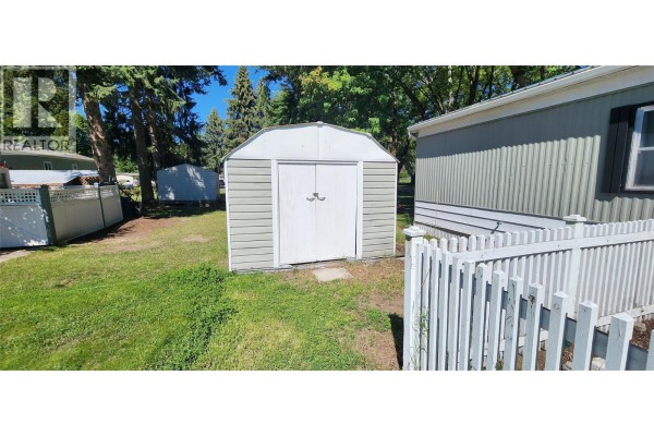A detached storage shed with double doors sits on a grassy lawn. - 5455 Almond Gardens Road Unit# A1, Grand Forks
