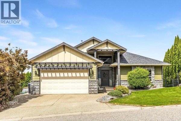 Front view of a two-story house with green siding, stone accents, a two-car garage, and landscaping. - 546 Gowen Place, Kelowna