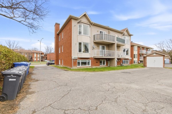 Side view of an apartment building with balconies, garage, and trash bins. - 547 Boul. Des Hautes-plaines, #1, Gatineau