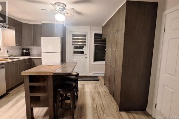 Modern kitchen with dark wood cabinets, white appliances, a kitchen island with stools, and wood-look flooring. - 547 Principale Street, Saint Basile