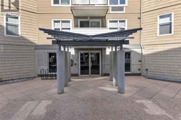 Covered entryway to the apartment building with concrete pillars and glass double doors. - 547 Yates Road Unit# 211, Kelowna