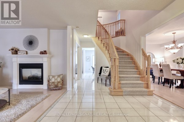 Spacious foyer with tiled floor, a curved staircase with carpeted steps, and a fireplace. - 5474 Middleport Crescent, Mississauga