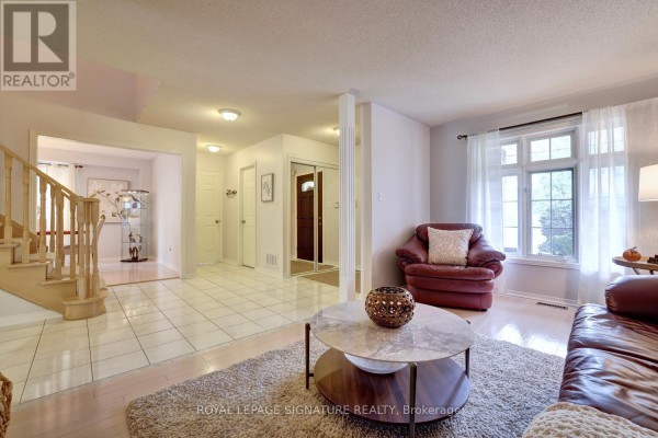Living room with a leather armchair, coffee table, and view into the foyer and dining area. - 5474 Middleport Crescent, Mississauga