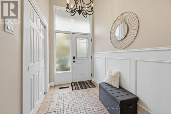 Entranceway with a white front door, beige tiled floor, and decorative circular mirror. - 5474 Schueller Crescent, Burlington