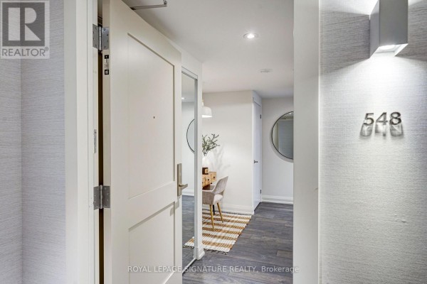 Interior view of an open apartment door showing a hallway with a small desk and mirror. - 548 - 26 Gibbs Road, Toronto