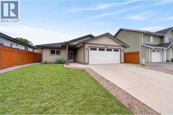 Empty room with beige walls, brown carpet, and a window with blinds overlooking trees. - 5480 Canoe Beach Drive Ne, Salmon Arm