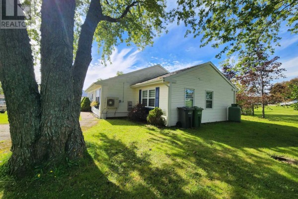 Rear exterior of the white bungalow, showing air conditioning unit, trash bins, and green lawn. - 549 Robert Clements Drive, Montague