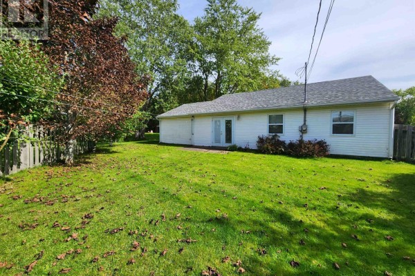 Backyard of the bungalow with a large grassy area, double glass doors, and a wooden fence. - 549 Robert Clements Drive, Montague