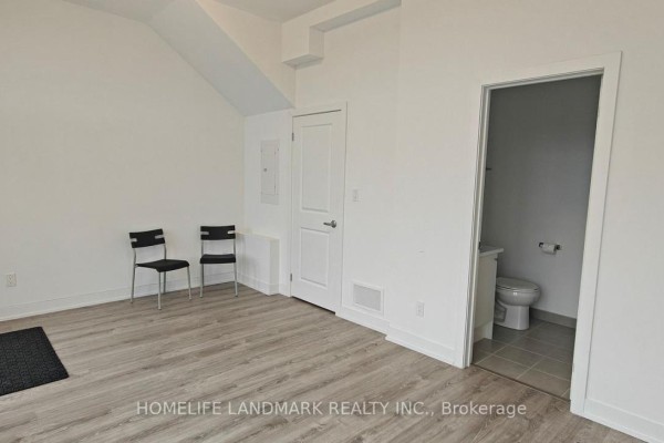 Empty room with neutral walls, hardwood flooring, and a door to another space. - 5494 Main Street, Whitchurch Stouffville