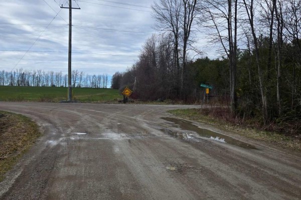 Gravel road intersection with a yellow sign and trees. Farmland is visible. - 5496 Fairvalley Road, Ramara Road, Ramara