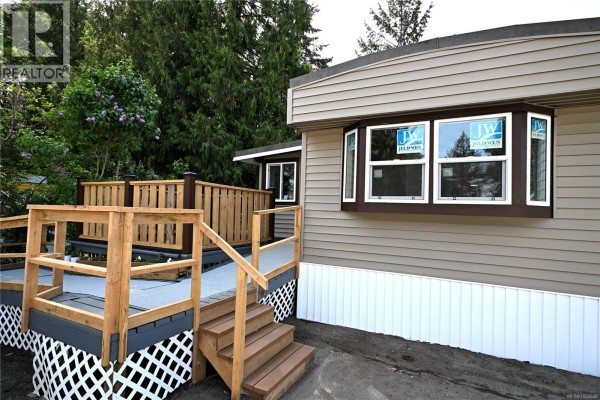 Exterior view of a mobile home with a wooden ramp and flower garden. - 55 1000 Chase River Rd, Nanaimo