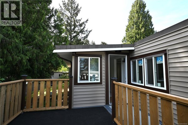 Close-up of a mobile home exterior with a wooden deck and bay windows. - 55 1000 Chase River Rd, Nanaimo