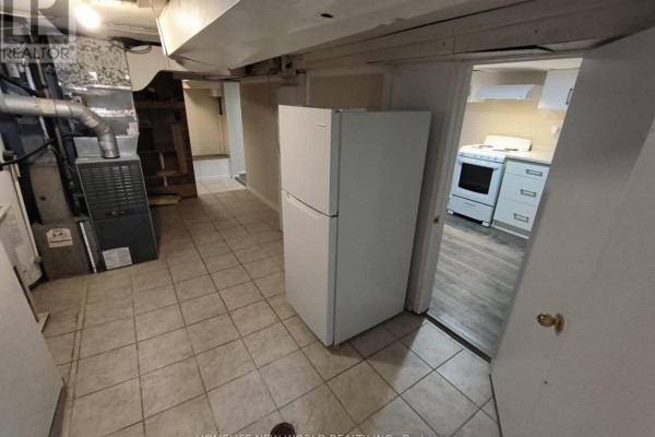 Laundry area with a white refrigerator and a furnace, next to an open doorway to the kitchen. - 55 Chamberlain B1 Avenue, Toronto
