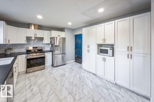 White kitchen with ample storage, stainless steel appliances, and a view of a blue door and staircase. - 55 Gladstone Cr, St  Albert