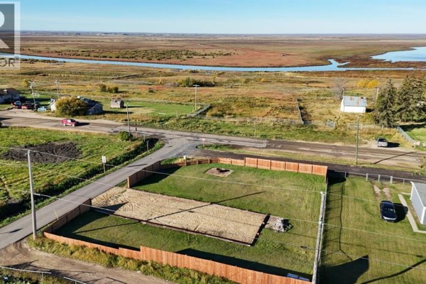 View of a fenced lot with a gravel pad and fire pit, with houses and a rural landscape in the background. - #55 Mission Street, Grouard