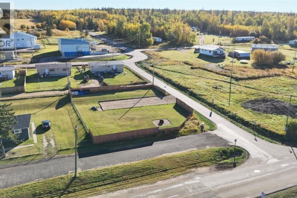 Street view showing a fenced lot with a gravel pad, surrounded by houses and a winding road. - #55 Mission Street, Grouard