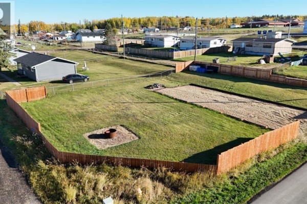 Close-up aerial view of a fenced lot with grass, a gravel pad, and a fire pit at #55 Mission Street. - #55 Mission Street, Grouard