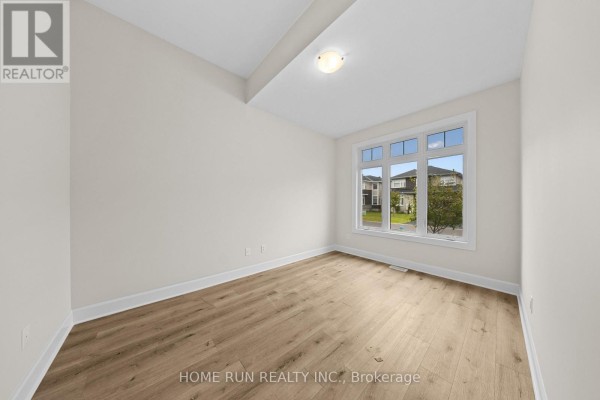 Empty room with light beige walls, light wood-look laminate flooring, and a large window with a suburban view. - 55 Robertson Lane, Carleton Place