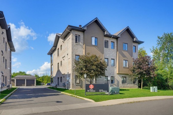 Apartment building exterior with lush green lawn and trees under a blue sky. - 55 Rue Du Britannia, #2, Gatineau