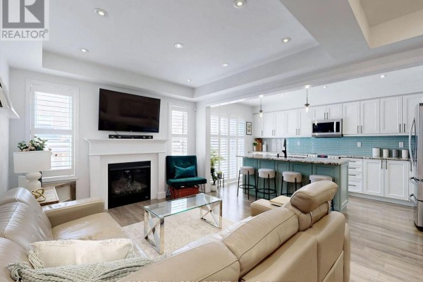 An open-concept living area and kitchen with a large sectional sofa, a kitchen island with stools, and light-colored flooring. - 55 Stocks Lane, Aurora