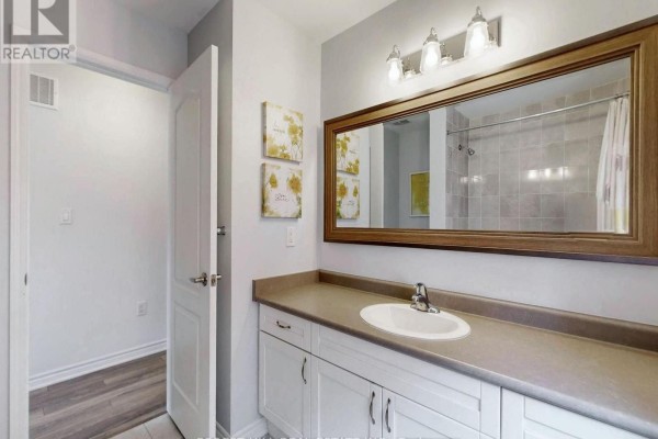 Bathroom vanity with dual sinks and large mirror, leading to wood-look floored room - 55 Stocks Lane Aurora