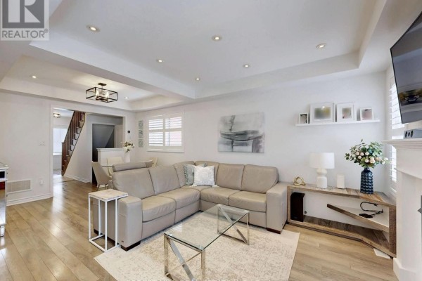 A living room with a fireplace, leather sofa, and a view into the open-concept kitchen with a large island. - 55 Stocks Lane, Aurora