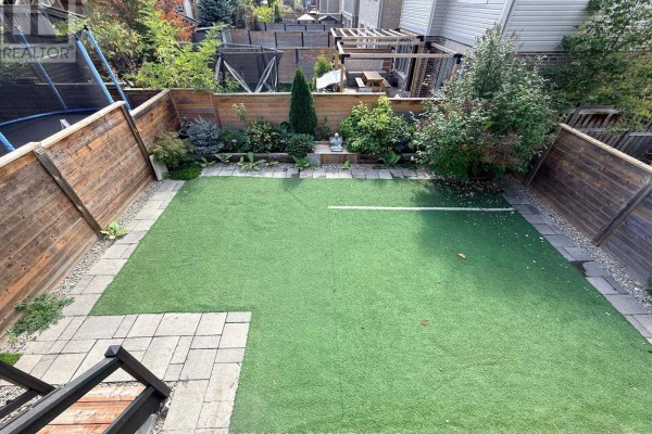 Backyard with artificial turf, wood fence, stone patio, and children's trampoline visible. - 55 Treetops Boulevard, New Tecumseth