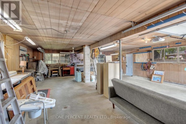 Interior of a workshop garage with concrete floor, wood paneled walls, and two garage doors. - 55 Young Street, Tillsonburg