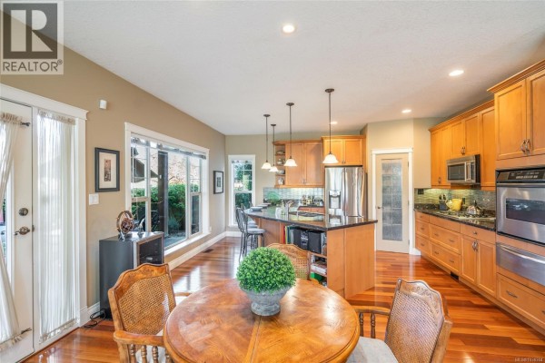 Covered patio with outdoor dining set, grill, and surrounding evergreen trees. - 550 Falcon Crt, Parksville