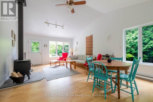 Open-concept living and dining area with light wood floors, vaulted ceiling, wood stove, and large windows. - 550 Huron Road N, South Bruce Peninsula