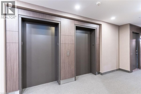 Hallway with three elevator doors and carpeted flooring in neutral tones - 550 North Service Road Unit# 516, Grimsby