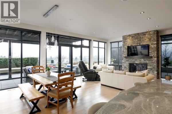 Open concept living and dining area with a wooden table, leather sofas, and stone fireplace. - 550 West Avenue Unit# 501, Kelowna