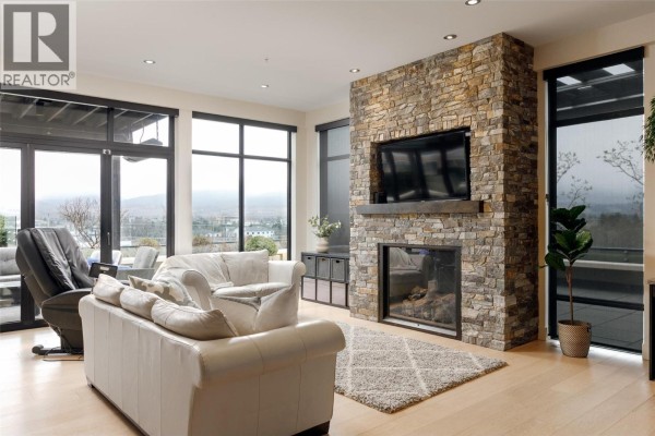 Living room with cream leather sofas, a stone fireplace, large windows, and a television. - 550 West Avenue Unit# 501, Kelowna