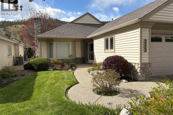 Side view of the beige house with a curved walkway, grass, and landscaping. - 550 Yates Road Unit# 212 Lot# 15, Kelowna