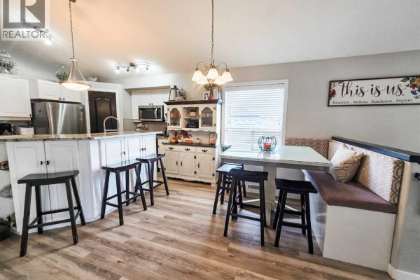 Kitchen island with black stools, a breakfast nook with bench seating, and white cabinetry. - 5501 17 Avenue, Edson