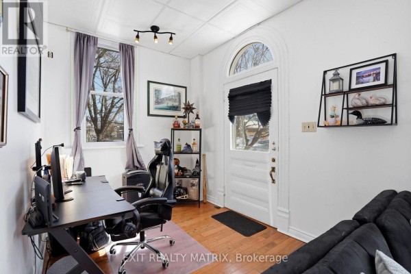 Living area with black sofa, desk, office chair, and a large arched window with purple curtains. - 5505 Osgoode Main Street, Ottawa