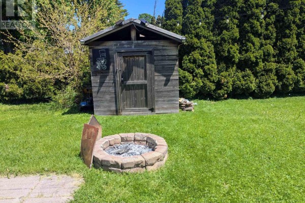 Wooden shed and stone fire pit in a grassy backyard with a thick hedge. - 551 15th Avenue, Hanover